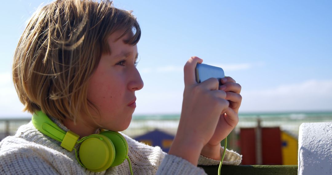 Child Wearing Green Headphones Using Smartphone at Beach - Free Images, Stock Photos and Pictures on Pikwizard.com