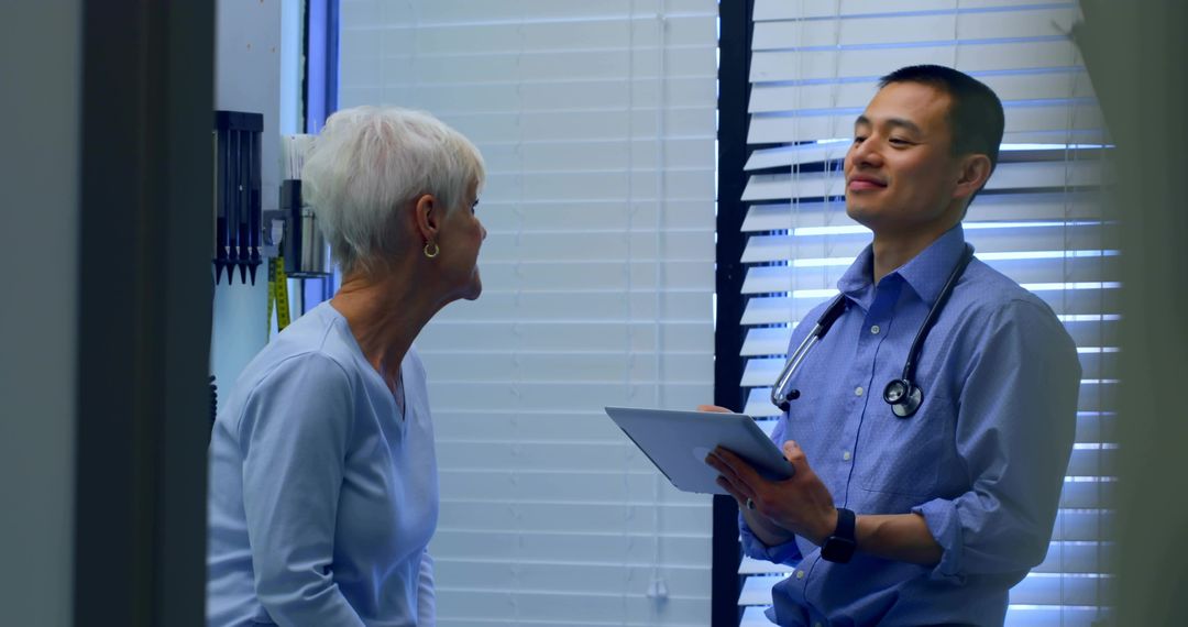 Primary Care Physician Consulting Senior Woman Using Tablet and Stethoscope in Clinic