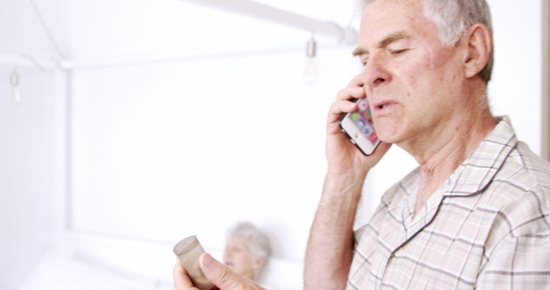 Senior Man Calling Doctor and Holding Medication Bottle in Bedroom - Free Images, Stock Photos and Pictures on Pikwizard.com