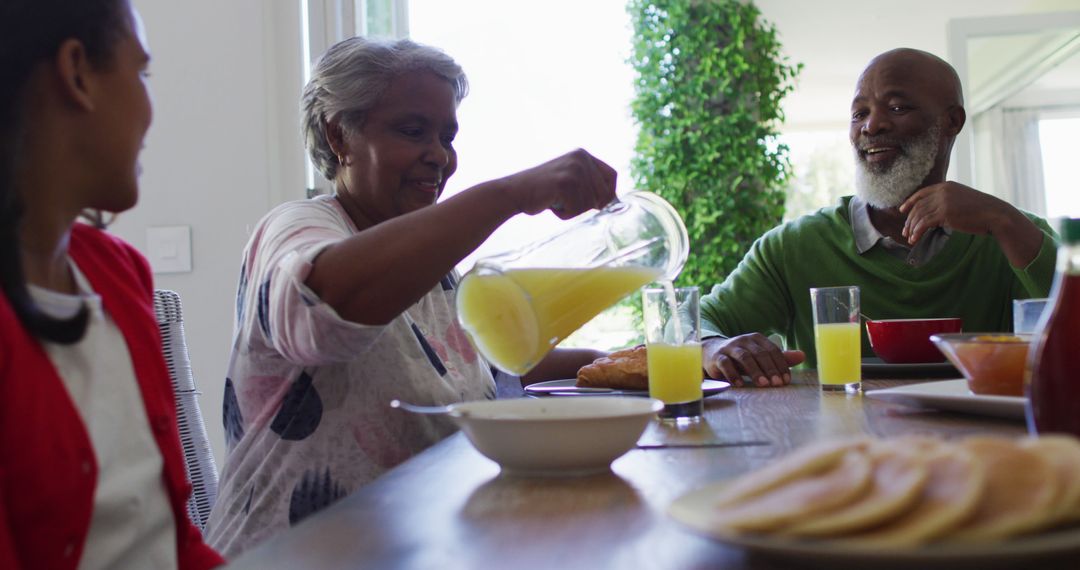 African american grandmother talking to her granddaughter while pouring juice in the glass - Free Images, Stock Photos and Pictures on Pikwizard.com