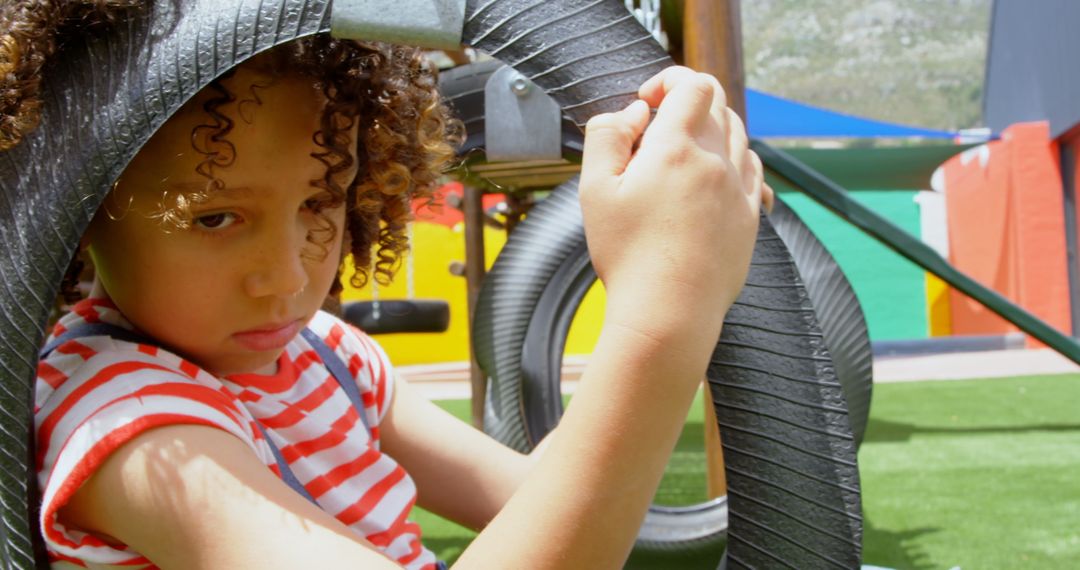 Thoughtful Child on Tire Swing in Colorful Playground