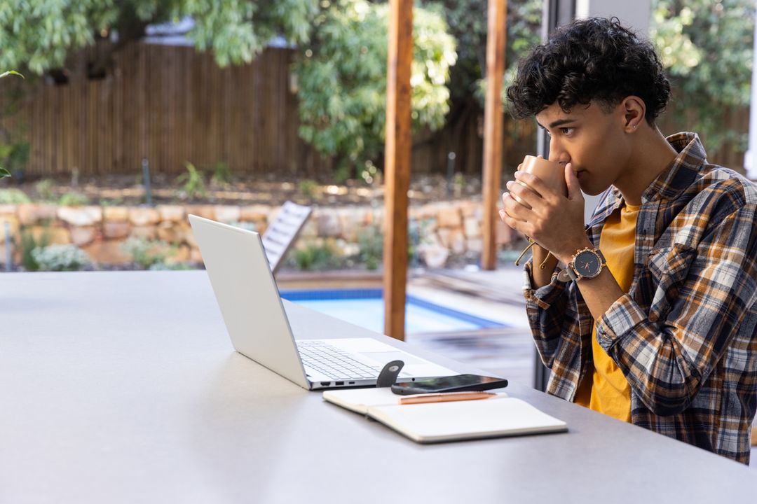 Young Man Relaxing with Coffee While Browsing Laptop Outdoors