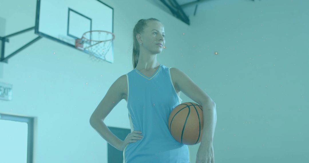 Confident Female Basketball Player Posing with Ball at Hip in Indoor Gymnasium Hoop Jersey