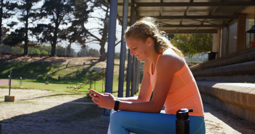 Teen Girl Relaxing on Bench Using Smartphone at Outdoor Sports Field - Free Images, Stock Photos and Pictures on Pikwizard.com