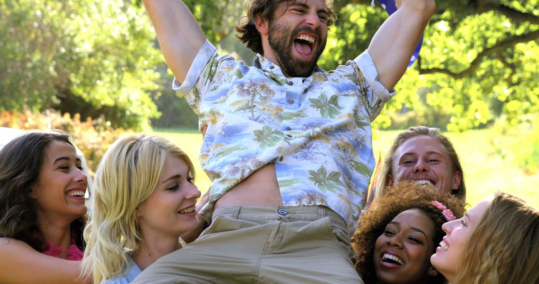 Friends Celebrating Lifts Happy Man in Park on Sunny Day - Free Images, Stock Photos and Pictures on Pikwizard.com