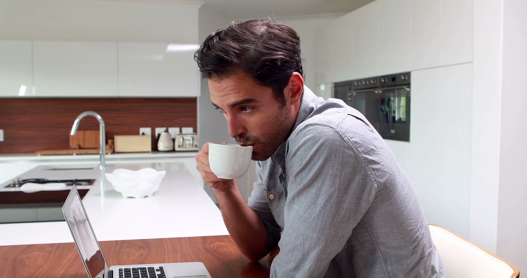 Young Man Drinking Coffee While Working at Home in Modern Kitchen - Free Images, Stock Photos and Pictures on Pikwizard.com