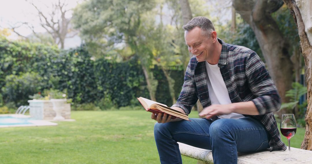 Middle-aged man reading book outdoors with wine glass and garden background - Free Images, Stock Photos and Pictures on Pikwizard.com