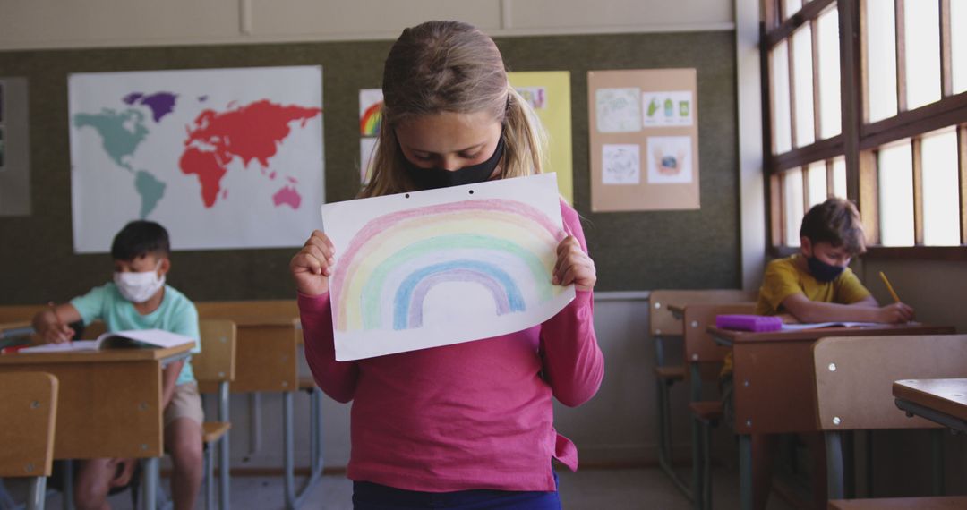 Girl Holding Rainbow Drawing in Classroom with Students Wearing Masks - Free Images, Stock Photos and Pictures on Pikwizard.com