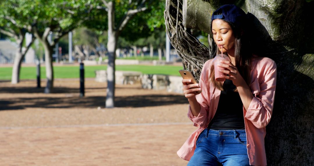 Young Woman Relaxing in Park with Phone and Drink - Free Images, Stock Photos and Pictures on Pikwizard.com