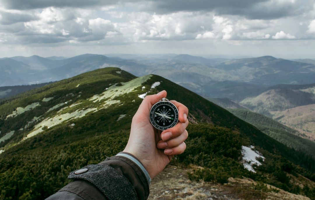 Hand Holding Compass Guiding Hiker on Mountain Ridge Overlooking Misty Mountain Range
