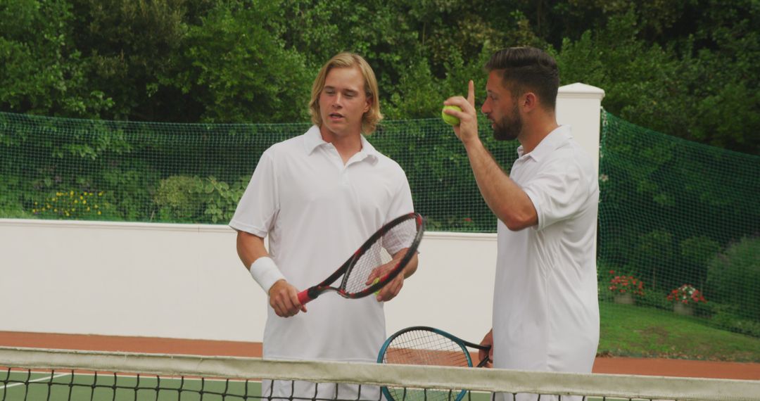 Two serious caucasian men holding tennis rackets and ball, talking at an outdoor tennis court - Free Images, Stock Photos and Pictures on Pikwizard.com