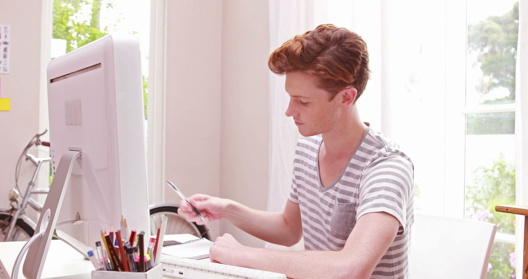 Young Redheaded Man Studying at White Desk in Bright Home Office - Free Images, Stock Photos and Pictures on Pikwizard.com