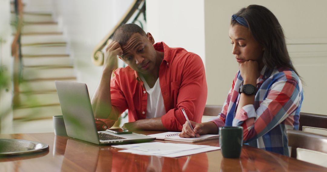 Stressed Couple Managing Home Finances with Laptop and Notebooks