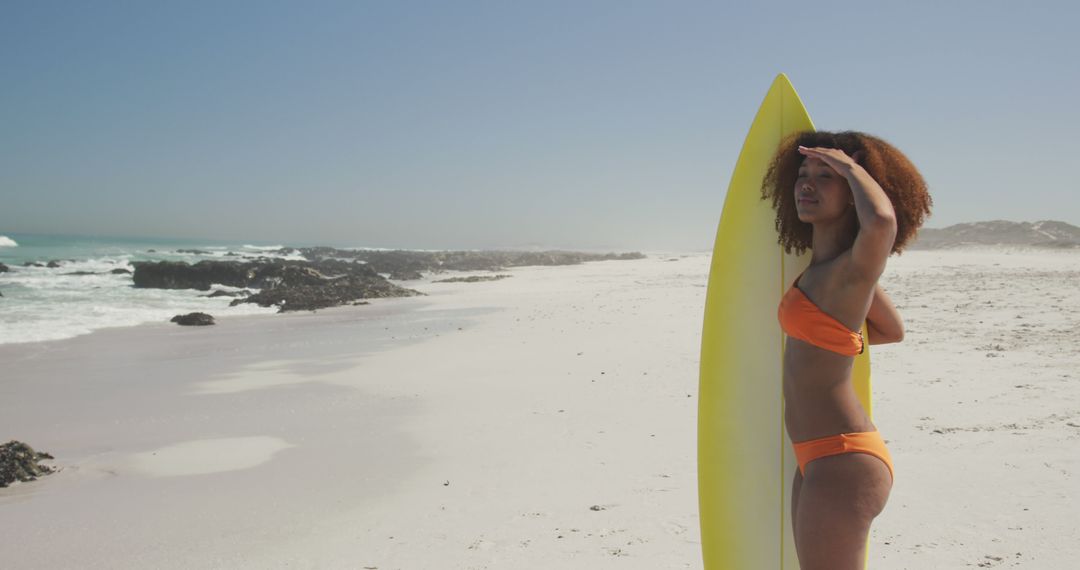 Young Woman Holding Surfboard on Sunny Beach, Looking at Ocean - Free Images, Stock Photos and Pictures on Pikwizard.com