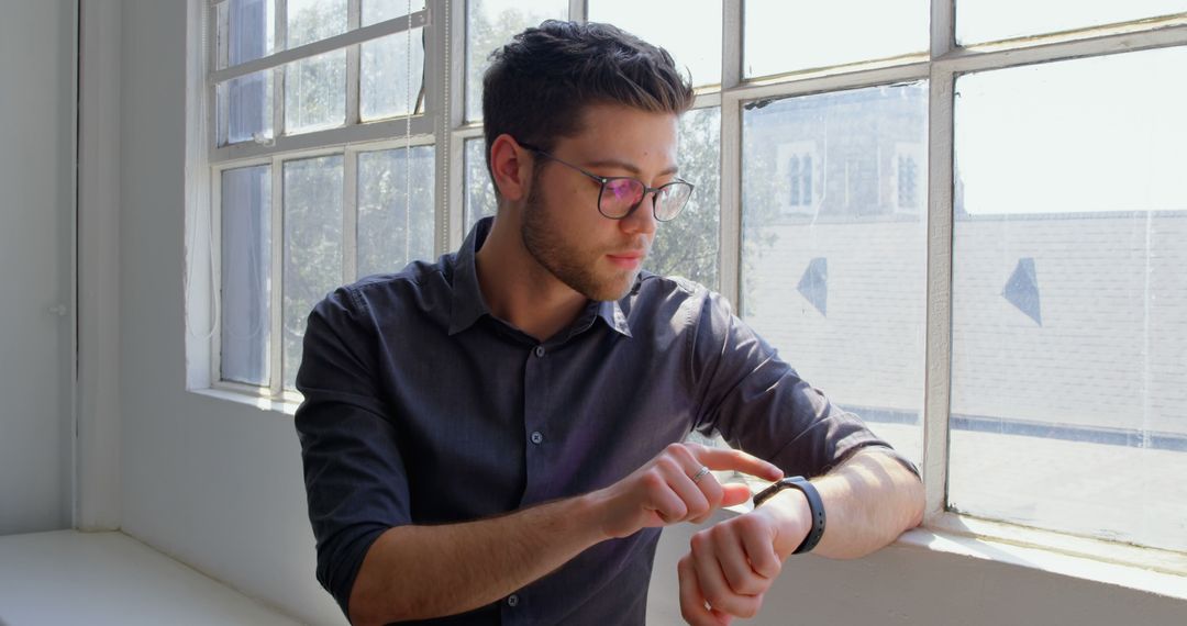 Young Professional Checking Smartwatch in Sunlit Office - Free Images, Stock Photos and Pictures on Pikwizard.com