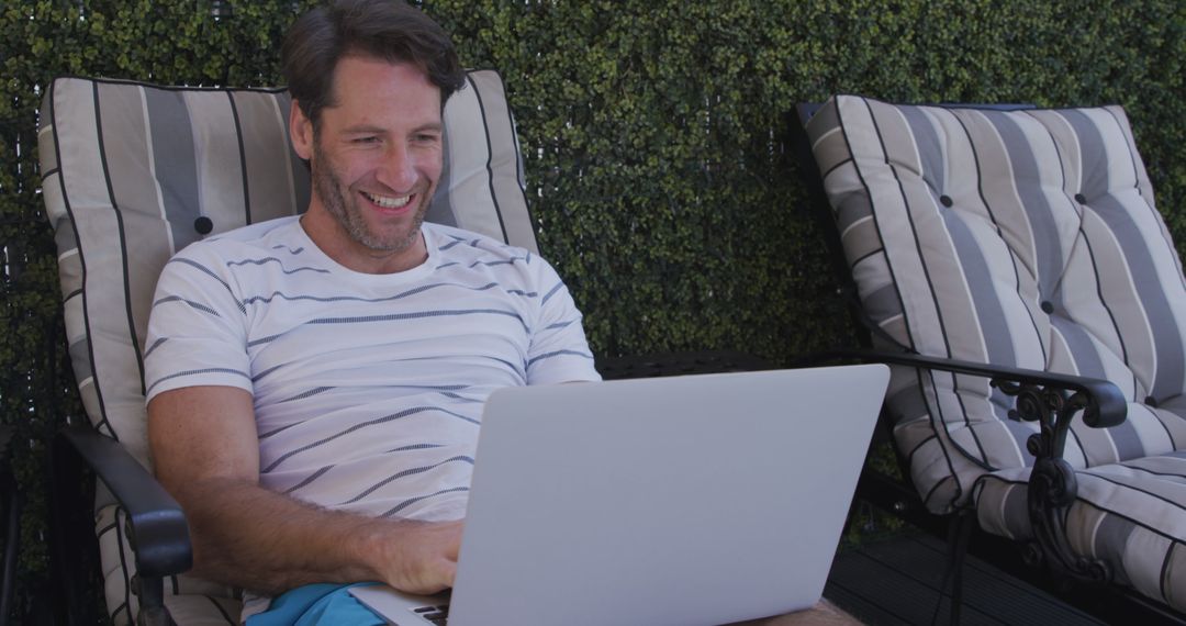 Smiling Man Using Laptop While Relaxing on Patio Loungers - Free Images, Stock Photos and Pictures on Pikwizard.com