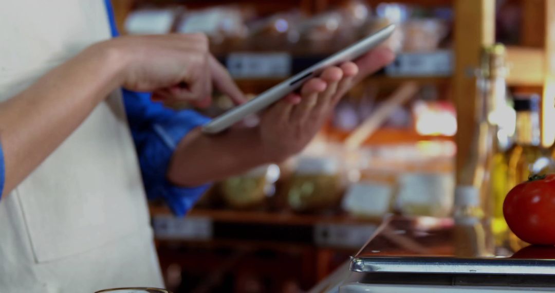 Aproned Worker Using Tablet in Grocery Store with Fresh Products