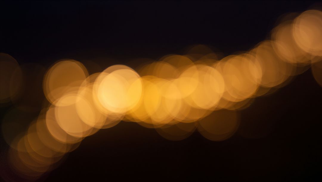 Glowing golden bokeh lights forming diagonal trail across deep dark night background