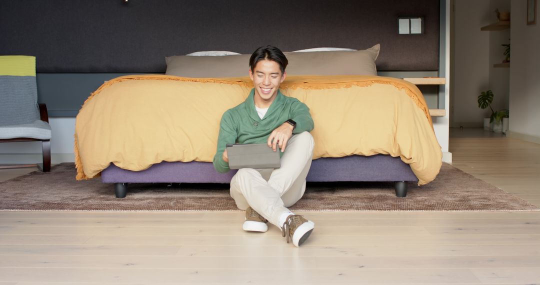 Asian Man in Bedroom Using Tablet for Leisure and Relaxation