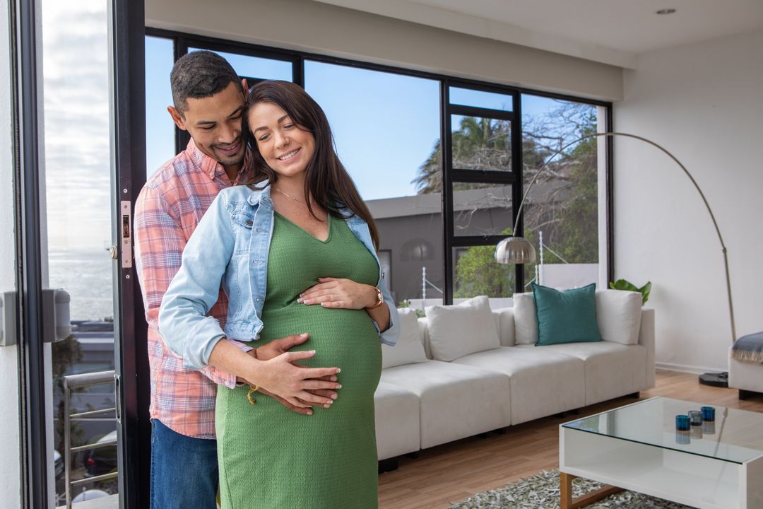Expecting Couple Embracing Joyfully by Ocean View Window