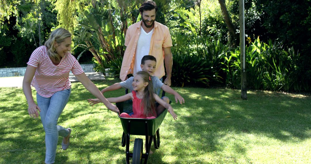 Happy Family Playing Outdoors with Wheelbarrow in Sunlit Garden - Free Images, Stock Photos and Pictures on Pikwizard.com