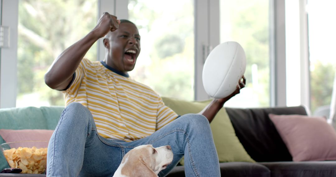 Excited Young Man Watching Rugby Game at Home with Dog - Free Images, Stock Photos and Pictures on Pikwizard.com