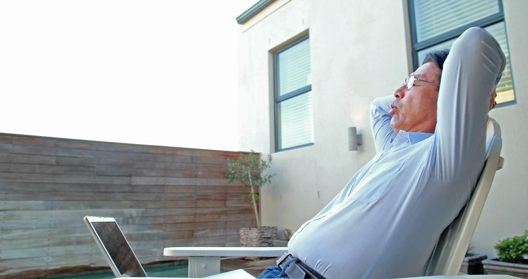 A middle-aged Asian man enjoys a leisurely break outdoors with his laptop nearby. - Free Images, Stock Photos and Pictures on Pikwizard.com