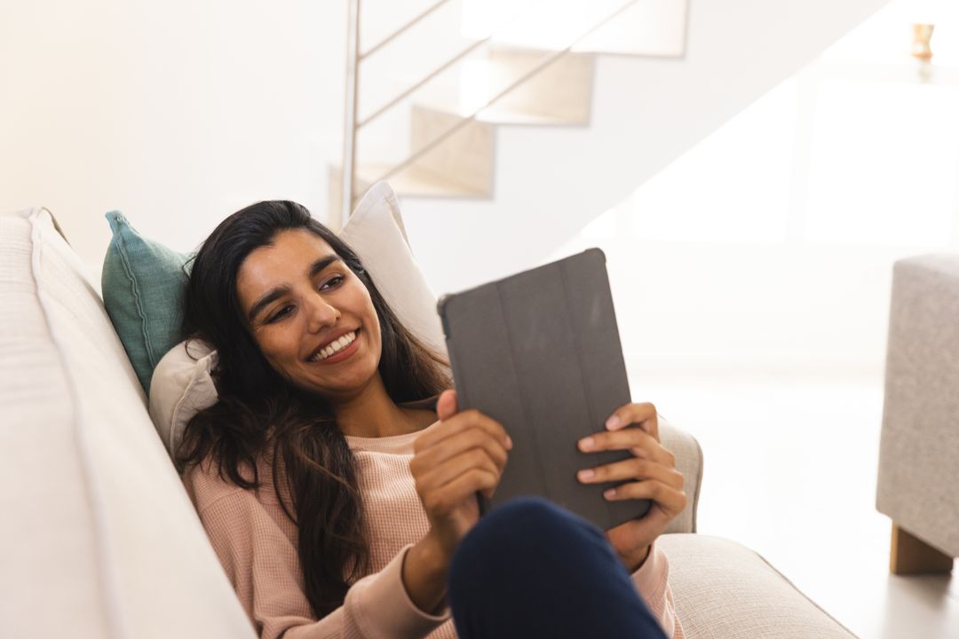 Asian Woman Relaxing and Smiling While Using Tablet on Sofa