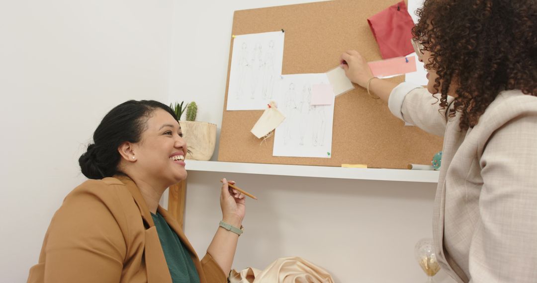 Female colleagues collaborating on fashion moodboard pinning fabric swatches and sketches