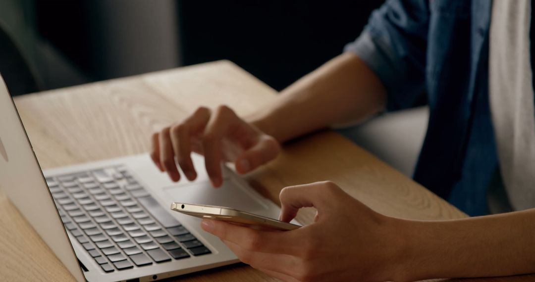 Person Multitasking Using Smartphone and Laptop at Desk