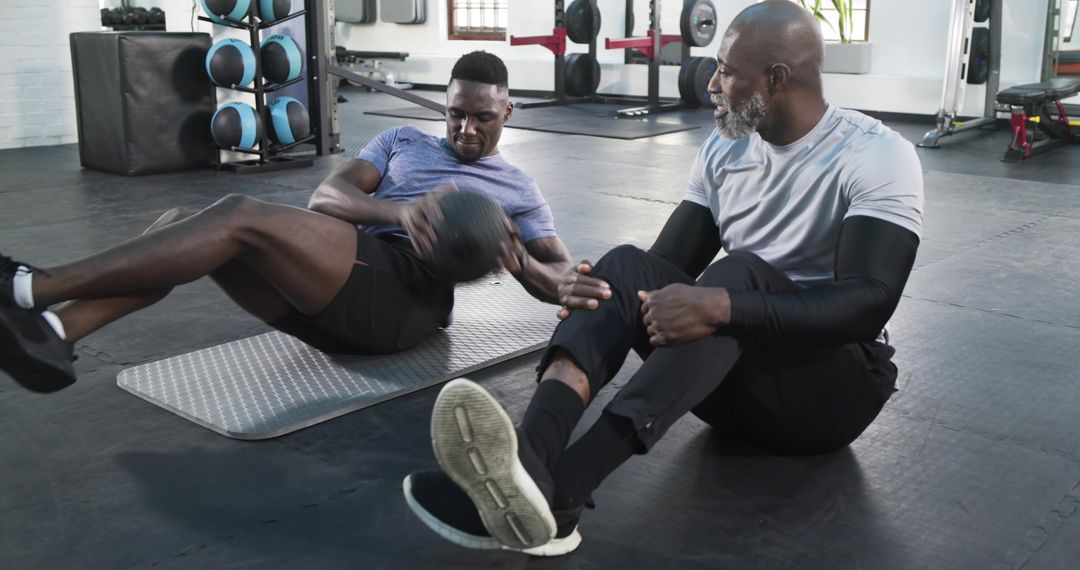 Trainer Guiding Client in Medicine Ball Exercise at Gym