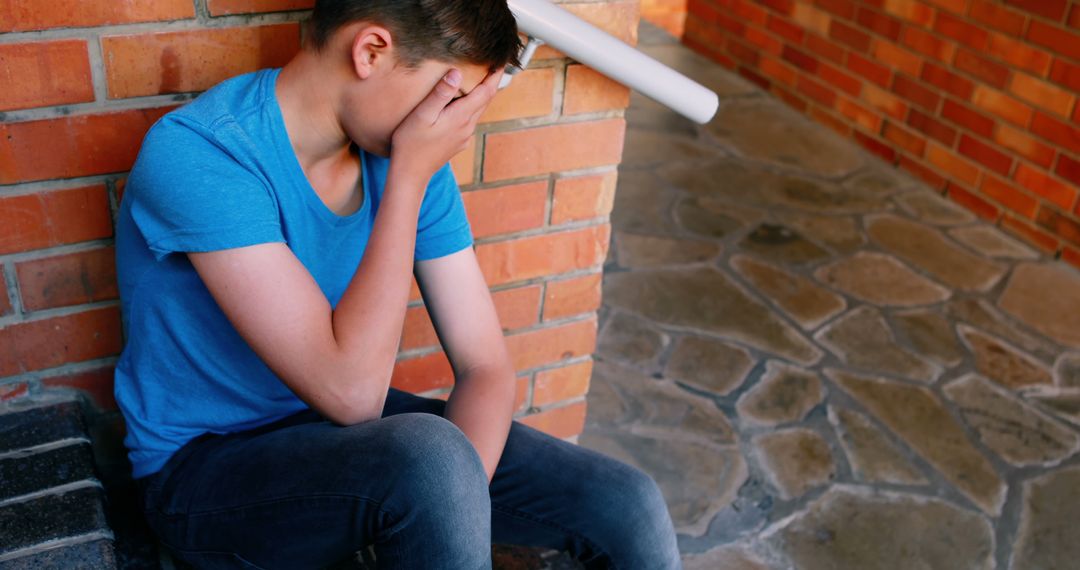 A troubled teenage boy sits alone, visibly distressed, against a brick wall. - Free Images, Stock Photos and Pictures on Pikwizard.com