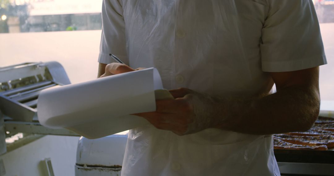 Man Writing on Clipboard in Commercial Kitchen - Free Images, Stock Photos and Pictures on Pikwizard.com