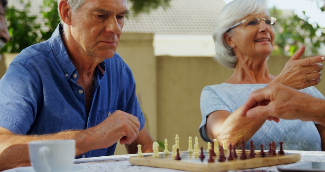 Senior Couple Reflecting on Move During Chess Game Outdoors