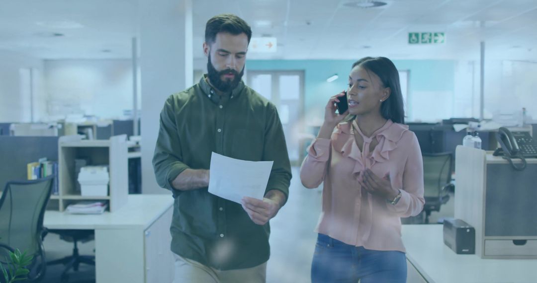 Two Coworkers Walking Through Open Office Consulting Document While Talking on Phone
