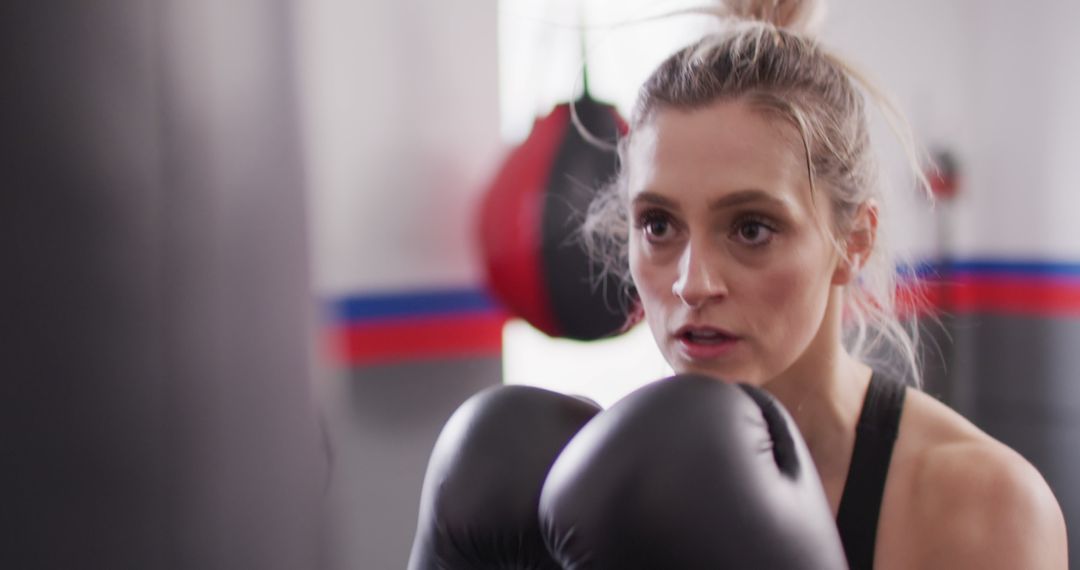 Image of confident, determined caucasian woman in boxing gloves training with punchbag at a gym - Free Images, Stock Photos and Pictures on Pikwizard.com