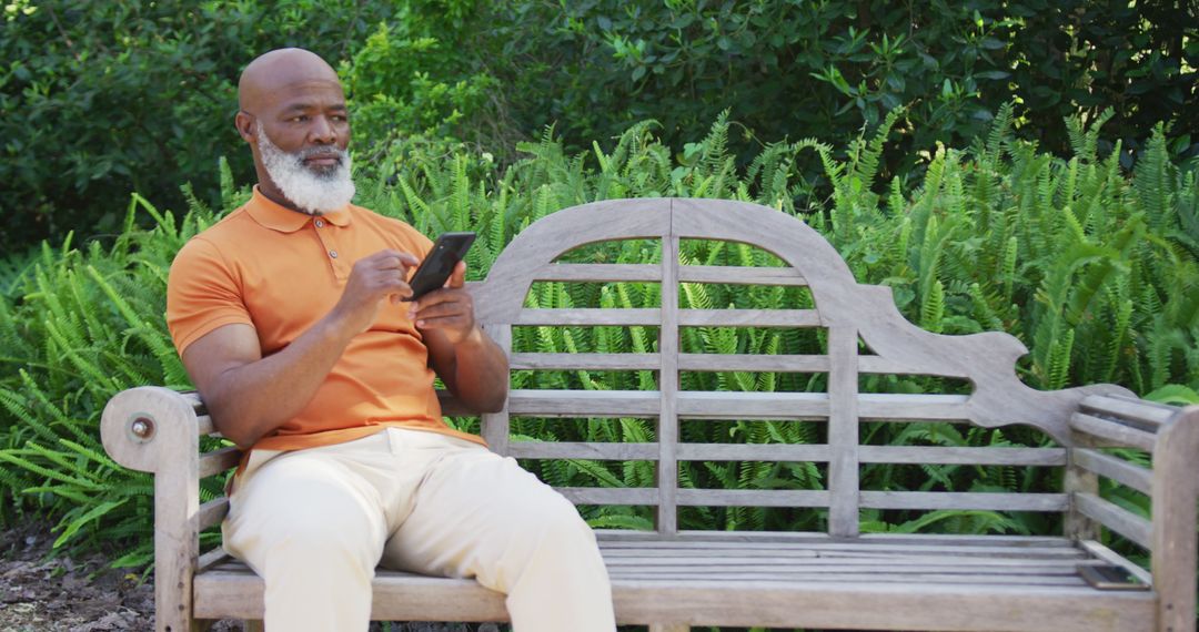 Senior Male Using Smartphone on Wooden Bench in Park Surrounded by Greenery - Free Images, Stock Photos and Pictures on Pikwizard.com