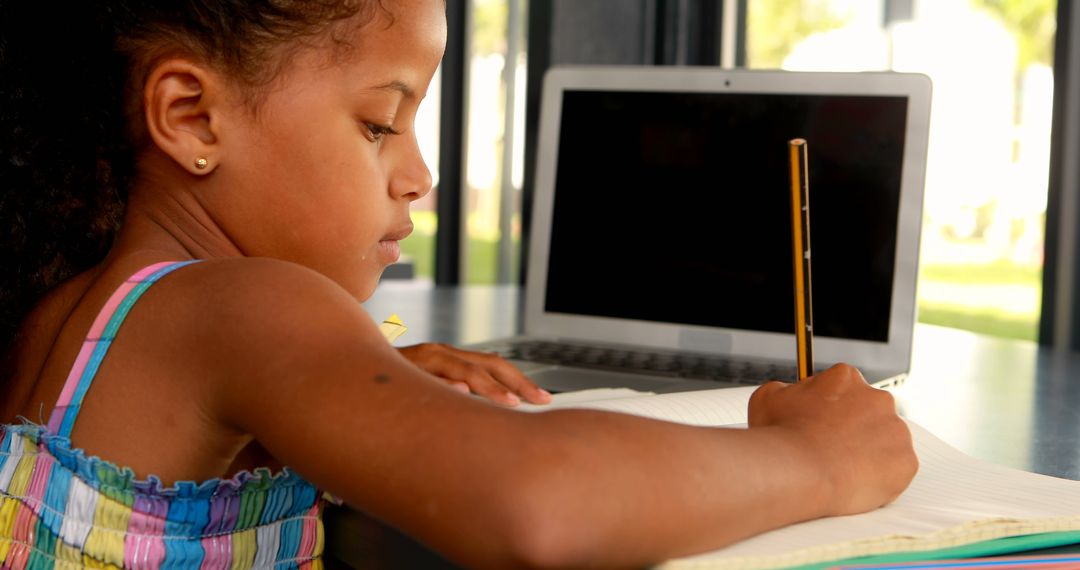 Focused Girl Writing with Laptop in Background - Free Images, Stock Photos and Pictures on Pikwizard.com