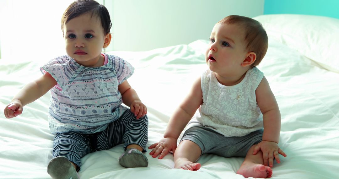 Two Adorable Babies Sitting on Bed in Bright Room - Free Images, Stock Photos and Pictures on Pikwizard.com