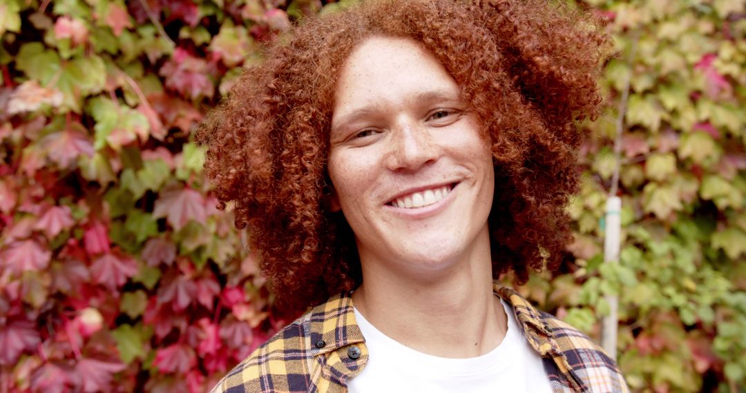 Smiling Young Person with Curly Hair Standing Outside with Colorful Foliage in the Background - Free Images, Stock Photos and Pictures on Pikwizard.com