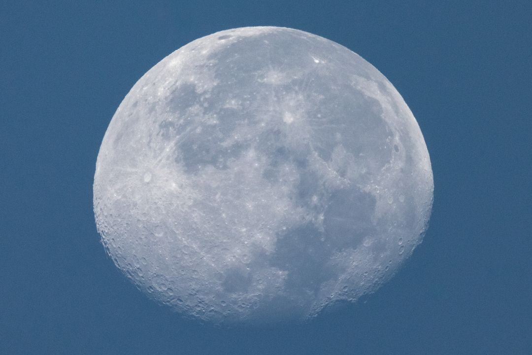 Close-up of white moon in daylight against universe blue sky