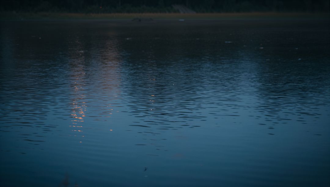 Twilight Lake Ripples Reflecting Warm Orange Lights on Calm Blue Water Surface