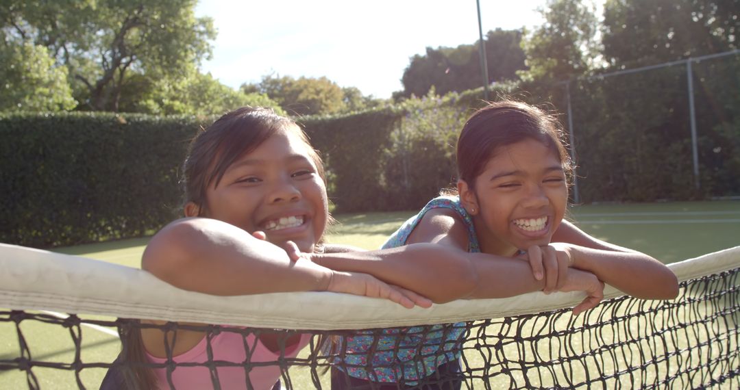 Smiling Girls Leaning on Tennis Net Enjoying Outdoors