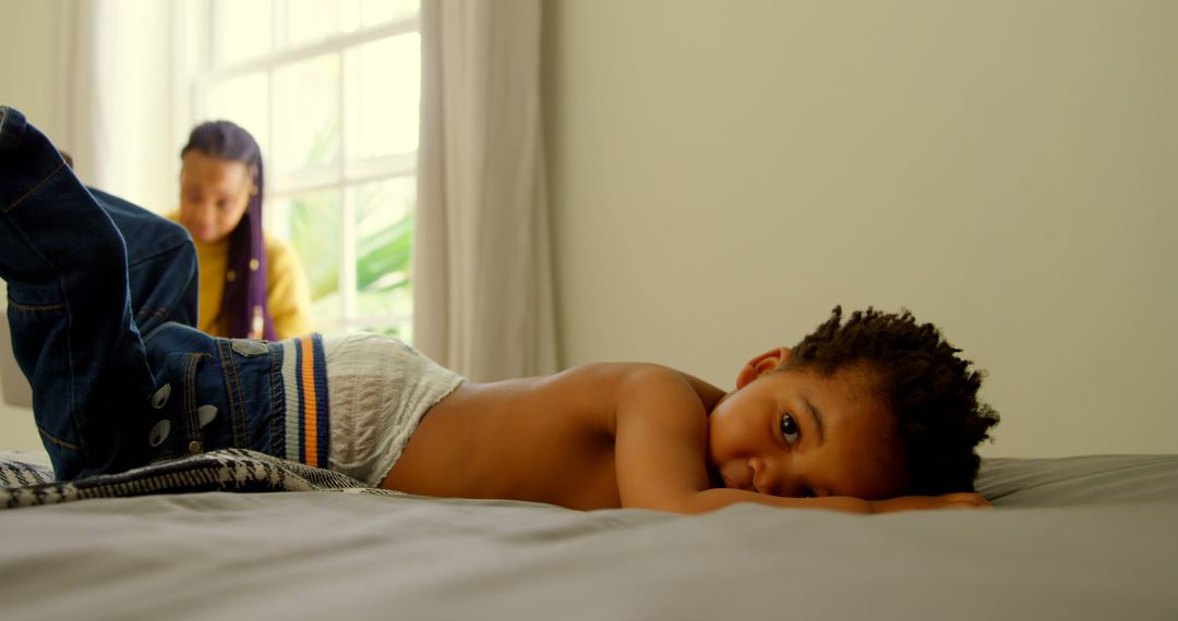 Child Resting on Bed with Parent in Background at Home - Free Images, Stock Photos and Pictures on Pikwizard.com