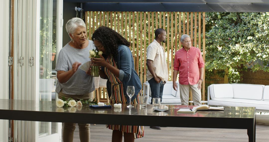 Senior woman guiding African American woman smelling bouquet on sunlit backyard patio