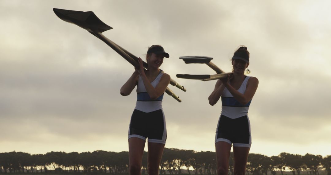 Two Female Rowers Carrying Oars at Sunset - Free Images, Stock Photos and Pictures on Pikwizard.com