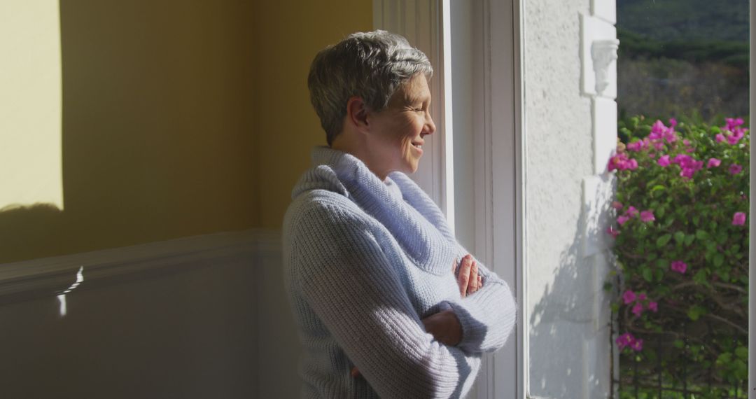 Smiling senior woman enjoying sunny view through window - Free Images, Stock Photos and Pictures on Pikwizard.com