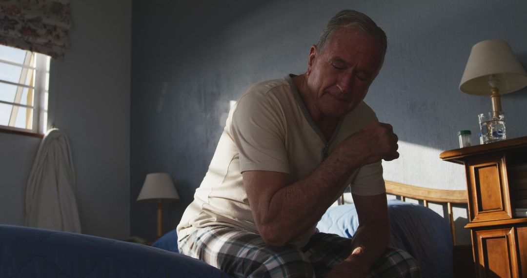 Elderly man experiencing shoulder pain while sitting on bed at home - Free Images, Stock Photos and Pictures on Pikwizard.com