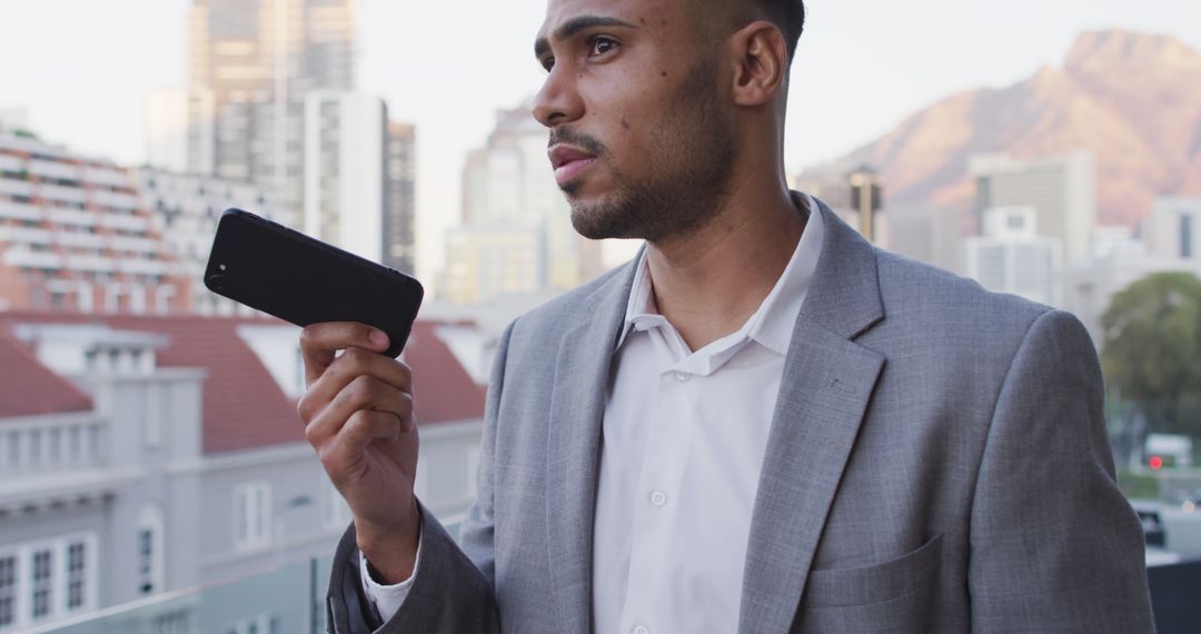 Businessman Using Smartphone for Voice Messaging with Urban Landscape Backdrop - Free Images, Stock Photos and Pictures on Pikwizard.com