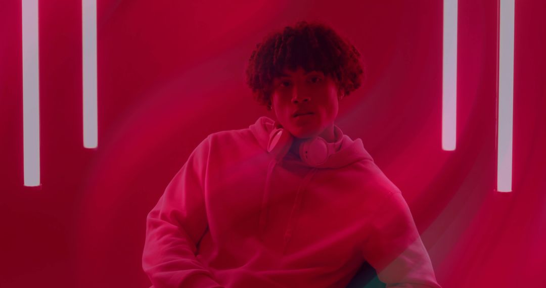 Man Relaxing in Hoodie with Headphones Amid Neon Glow